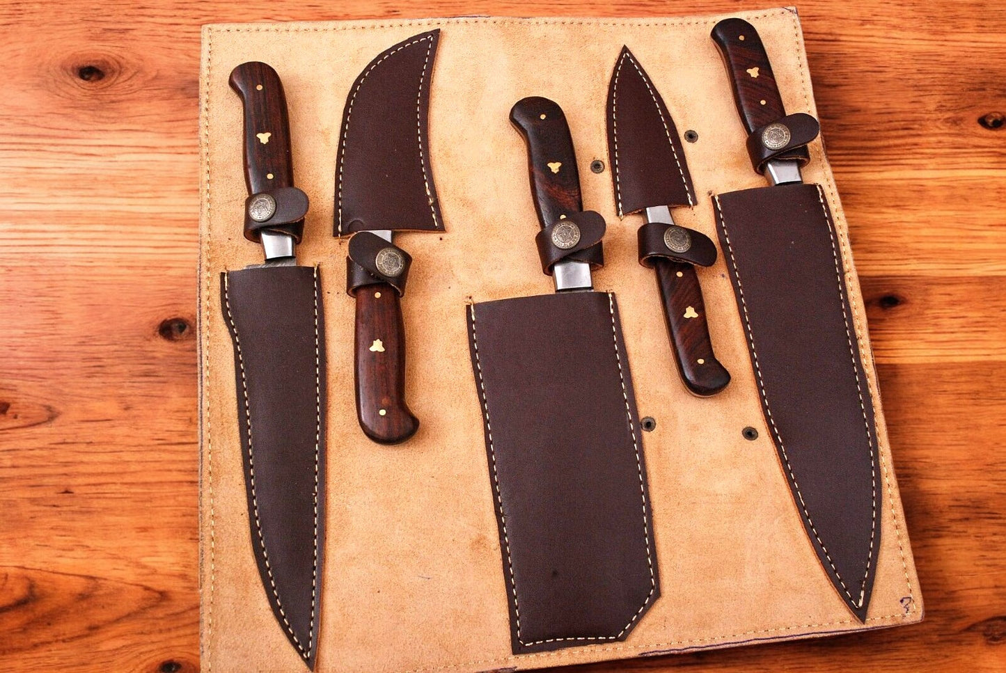 Set of custom handmade Damascus kitchen knives arranged in a leather roll.
