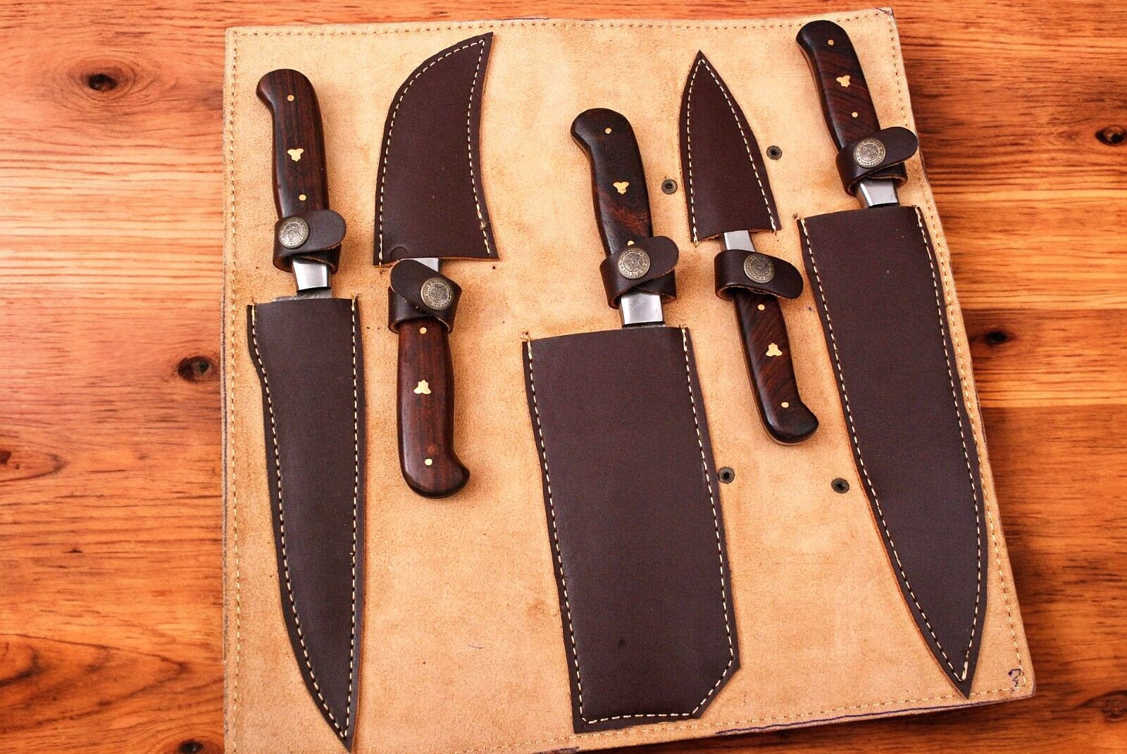 Set of custom handmade Damascus kitchen knives arranged in a leather roll.
