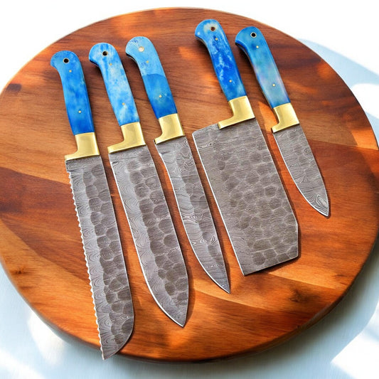 Full set of custom Damascus kitchen knives displayed on a wooden table.
