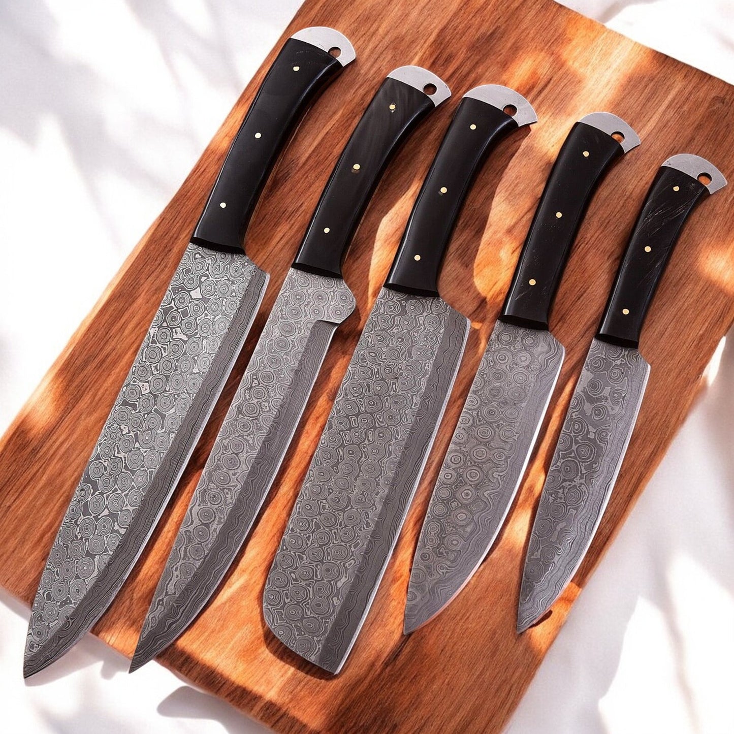 Handmade kitchen knife set displayed on a wooden surface.
